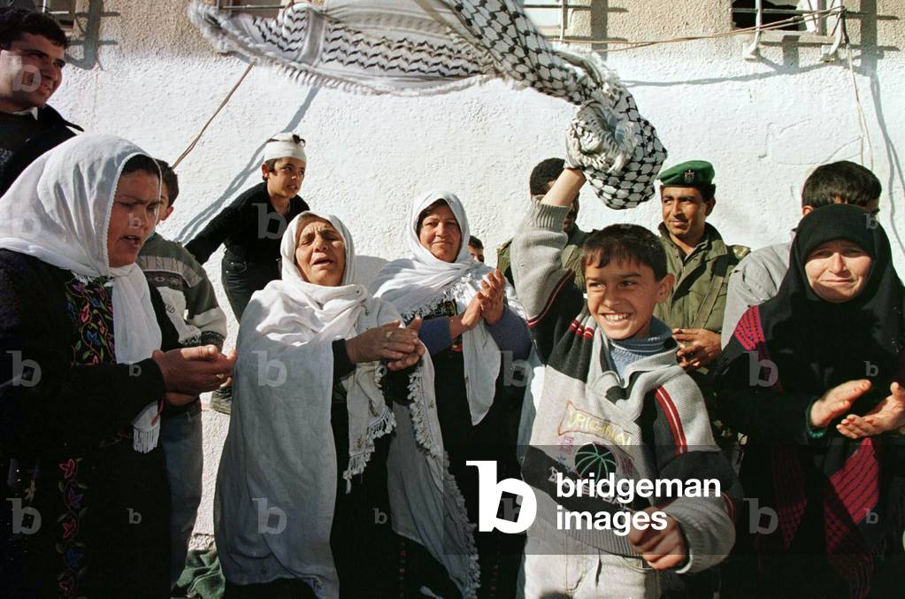 Image of a palestinian boy waves a kufia in the air as