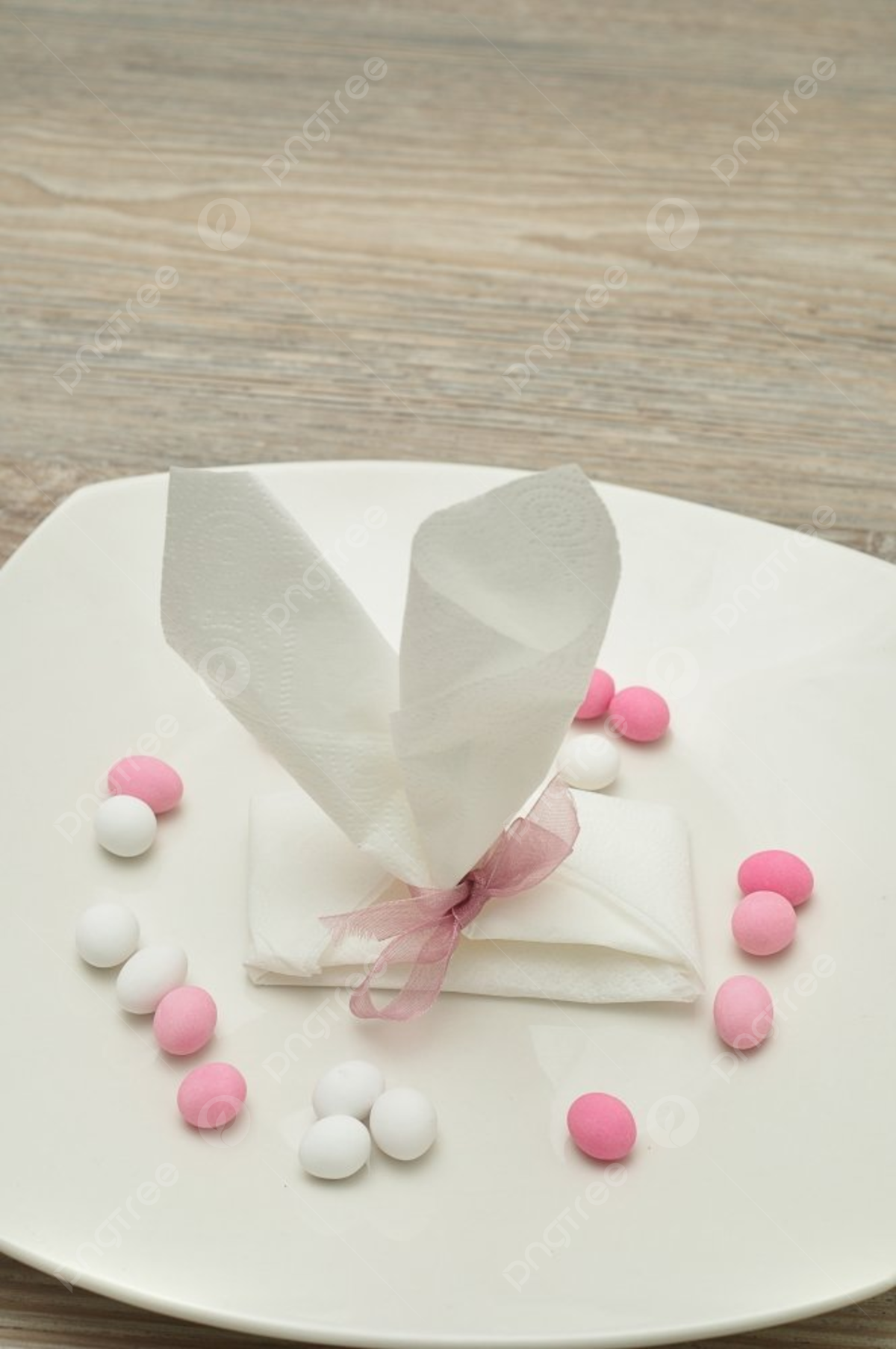An easter place setting with the napkin in the shape of bunny ears displayed in a plate with pastel color candy photo background and picture for free download
