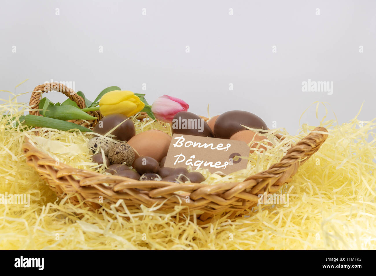 Joyeuses pãques is happy easter written in french on a label in a wicker basket filled with eggs and tulips stock photo