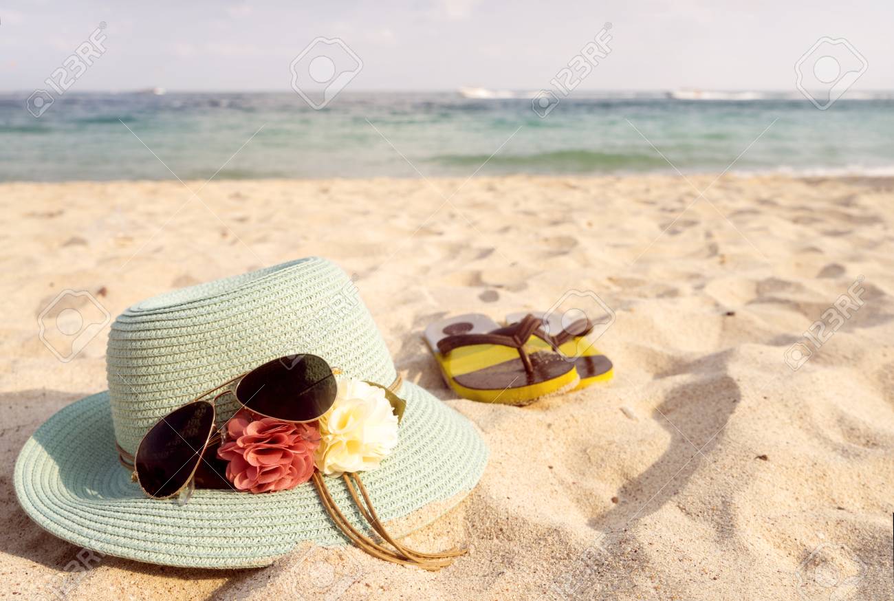 Summer vacation concept with straw hat sunglasses and flip flops on sandy tropical beach